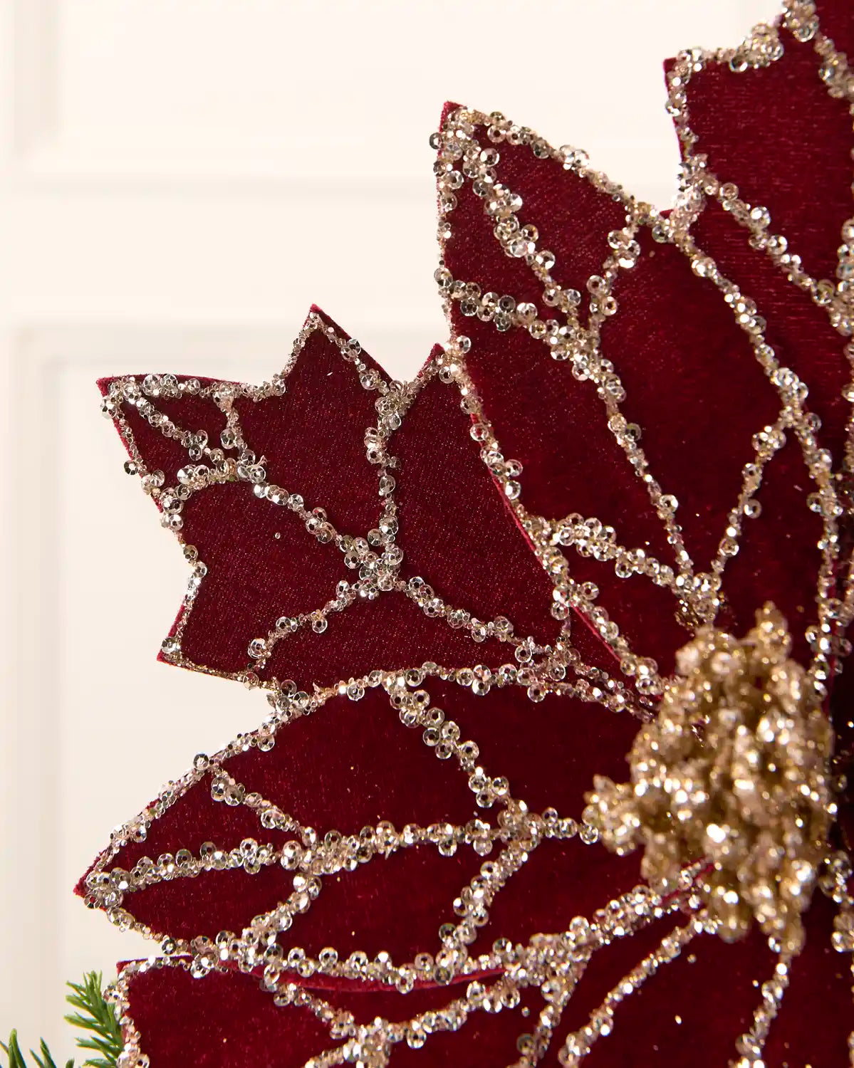 A close-up of a Burgundy poinsettia-style decorative flower with silver rhinestone trim and a gold glitter center, shown against a light neutral background.