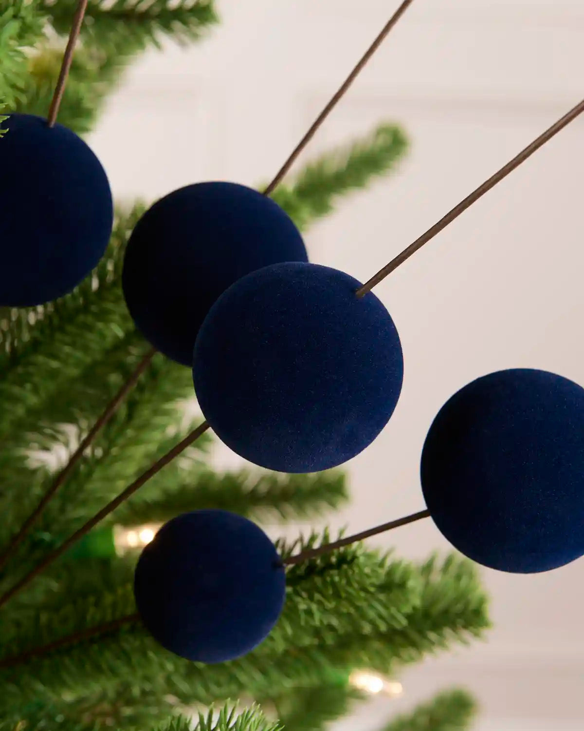 A close-up of a Christmas tree decorated velvet bauble pick with five navy blue velvet ball ornaments on thin stems
