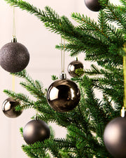 A close-up of a Christmas tree decorated with shiny metallic and glittery Espresso spherical ornaments hanging from green branches against a soft light background.