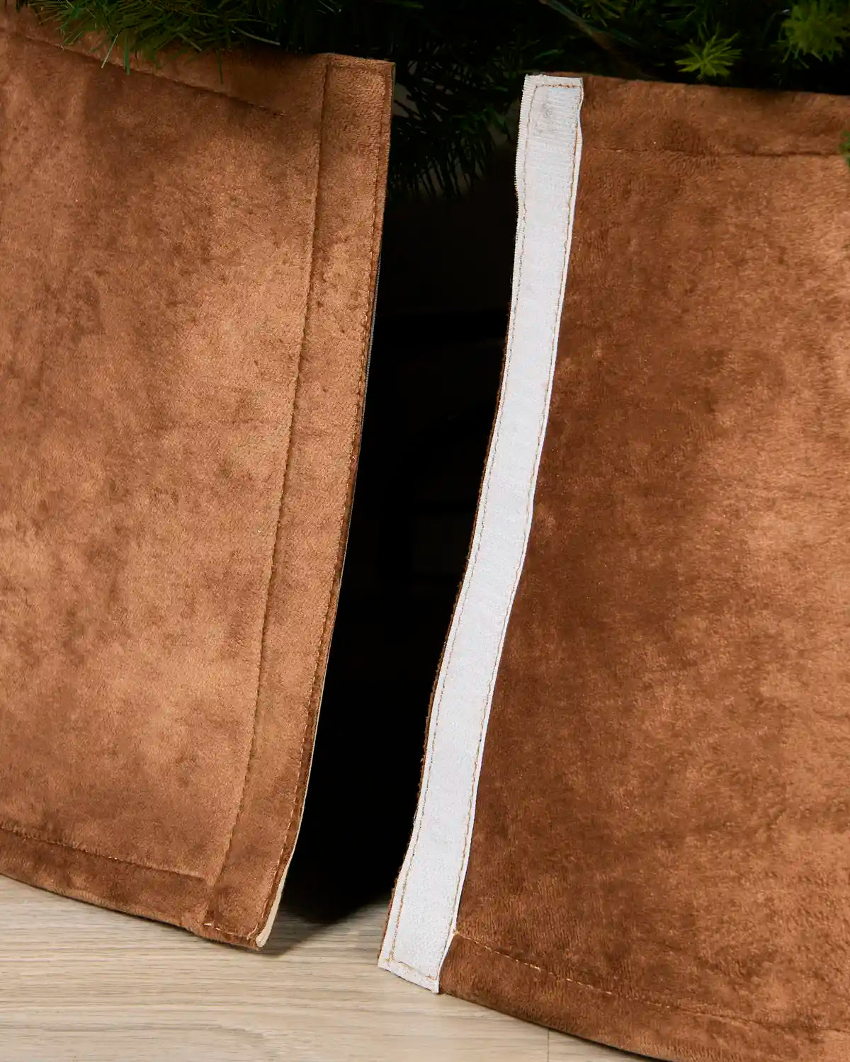 A close-up of a Mocha coloured velvet Christmas tree skirt with a white trim, shown partially pulled open to reveal its shape and texture.