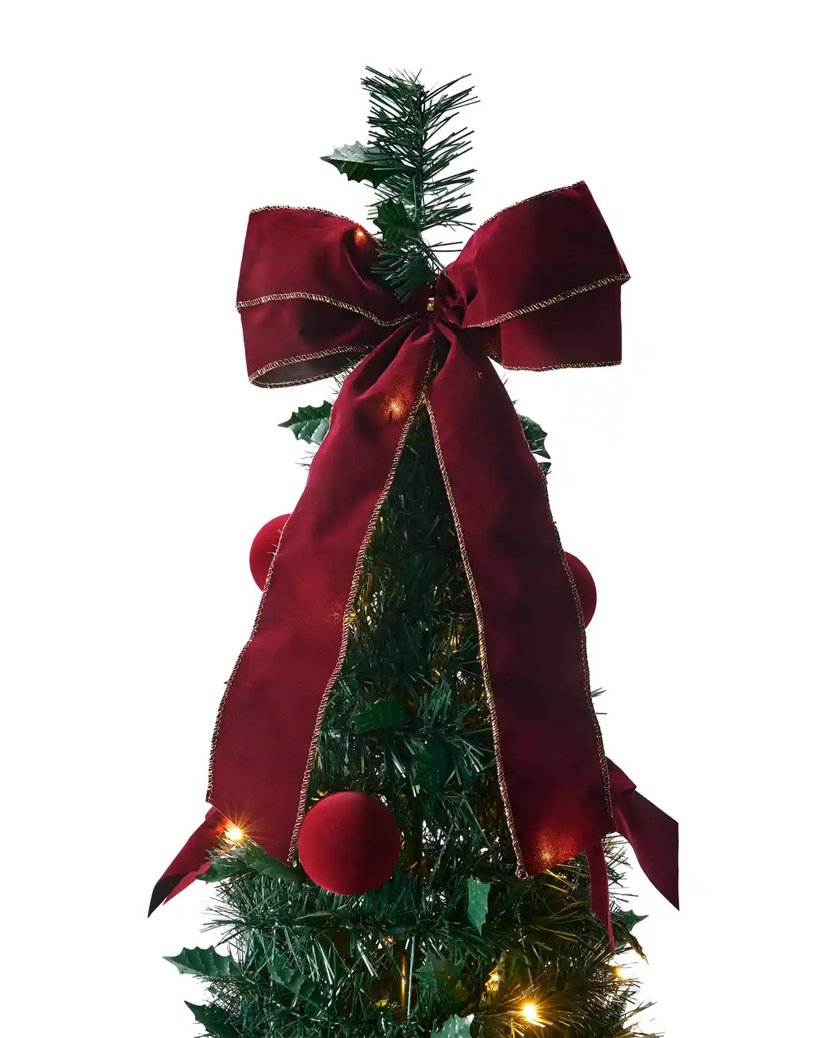 A close-up of a dark red fabric bow tied around a green artificial Christmas tree with small warm lights and holiday decorations.
