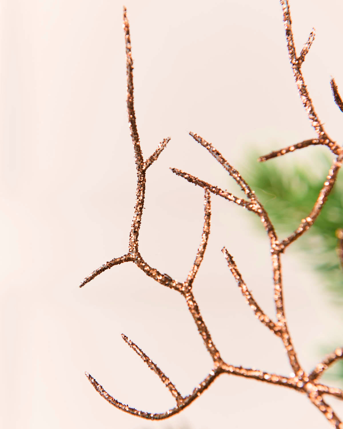 A close-up of a decorative branch-like ornament with glittery Mocha branches against a soft cream background with a hint of green foliage.