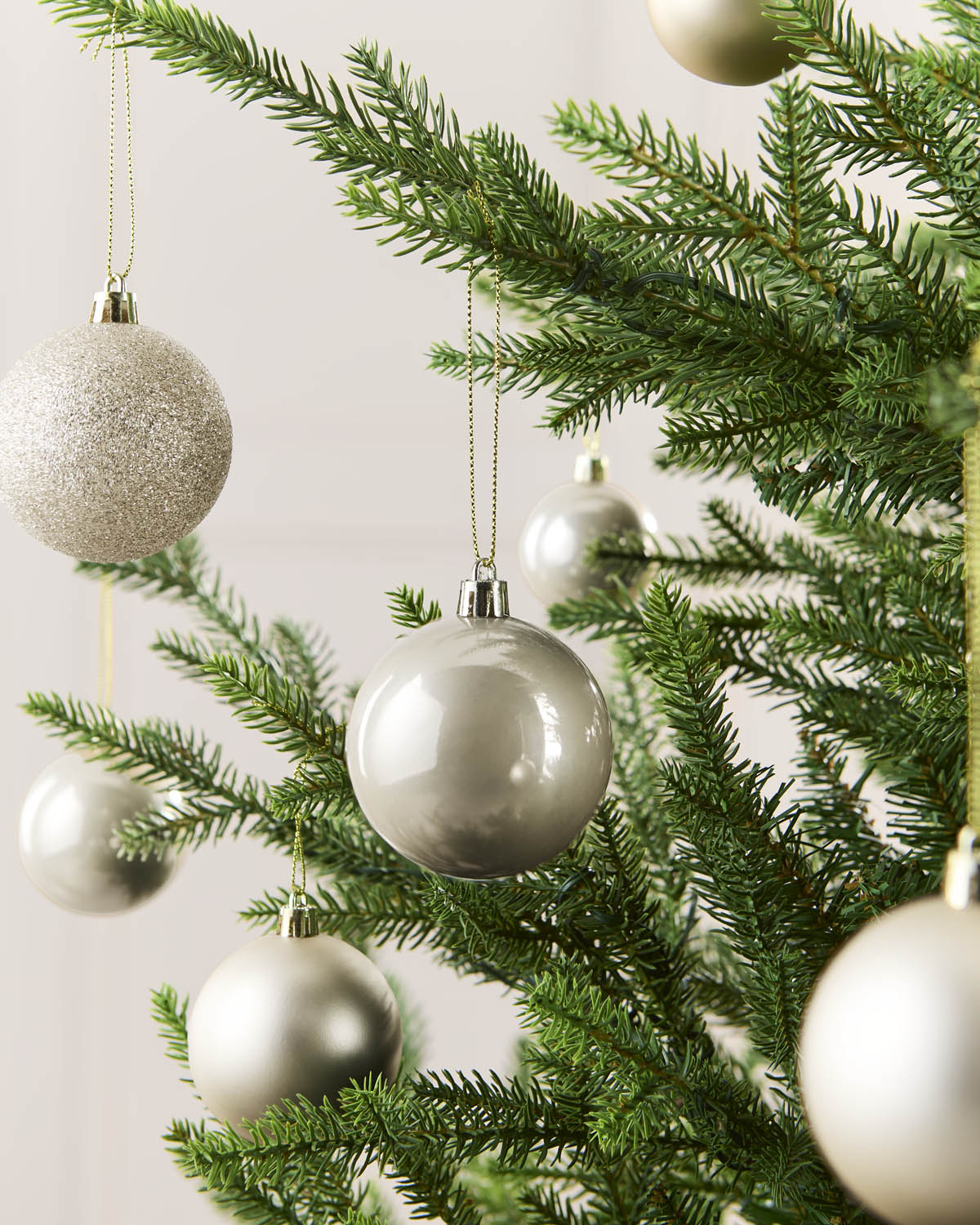 Seven Latte Christmas tree ornaments hanging from green pine branches against a soft light background.