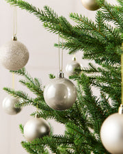 Seven Latte Christmas tree ornaments hanging from green pine branches against a soft light background.