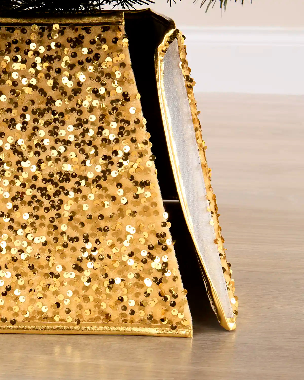 A close-up of a gold sequined tree collar with a white inner Velcro strip, shown standing on a light wood floor.