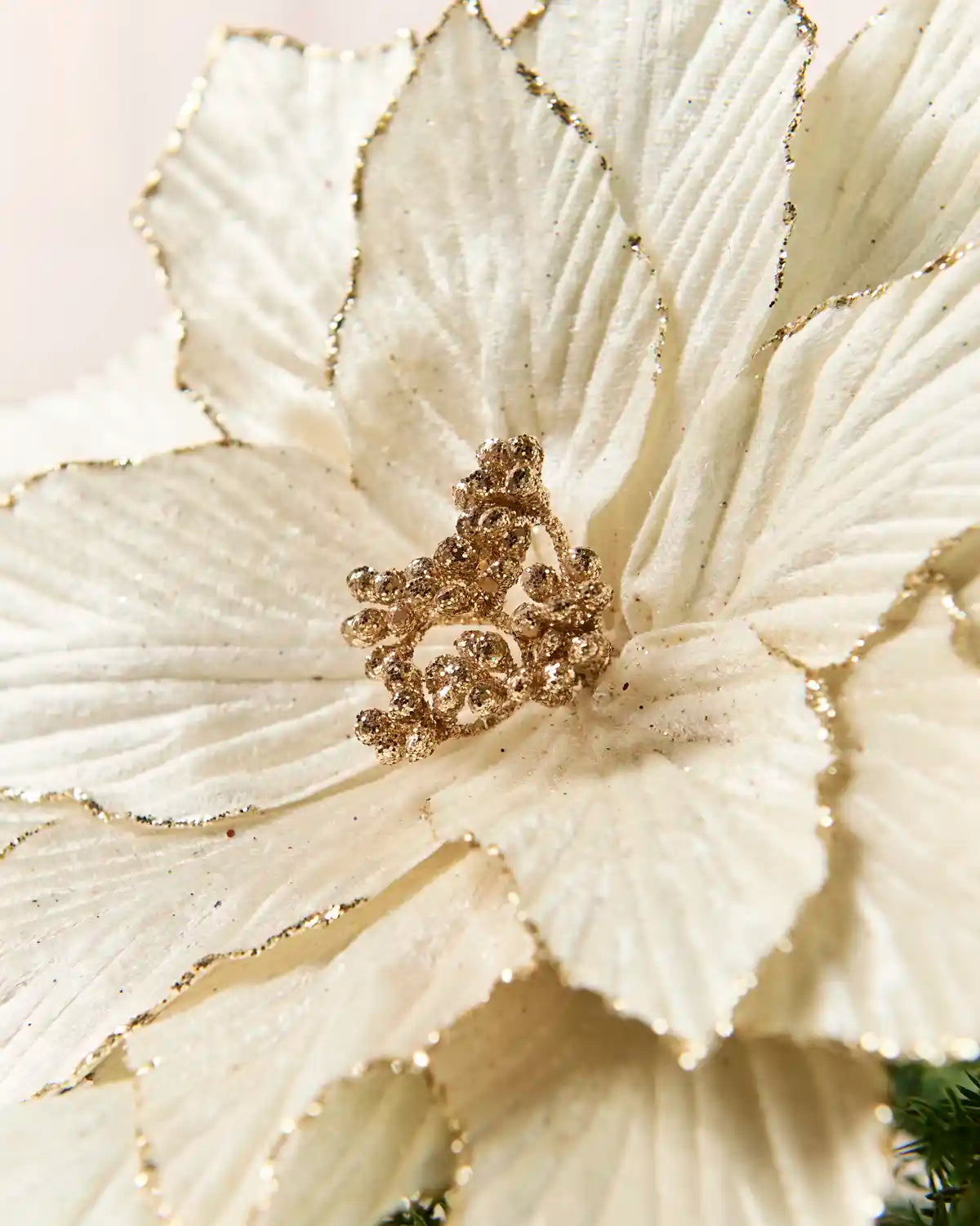 A close-up of a large cream artificial flower with textured petals and metallic gold glitter accents along the edges and centre.