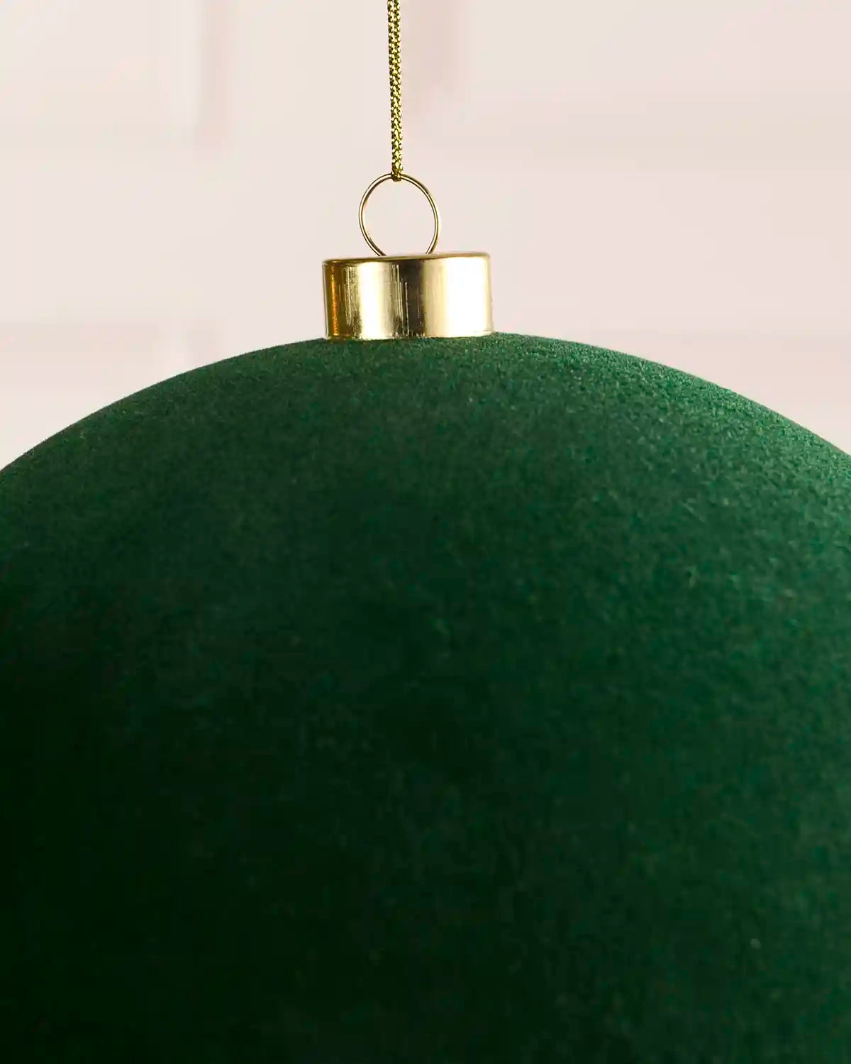 A close-up of a large sage green spherical ornament with a gold cap and hanging loop, on a thin gold chain against a light background.