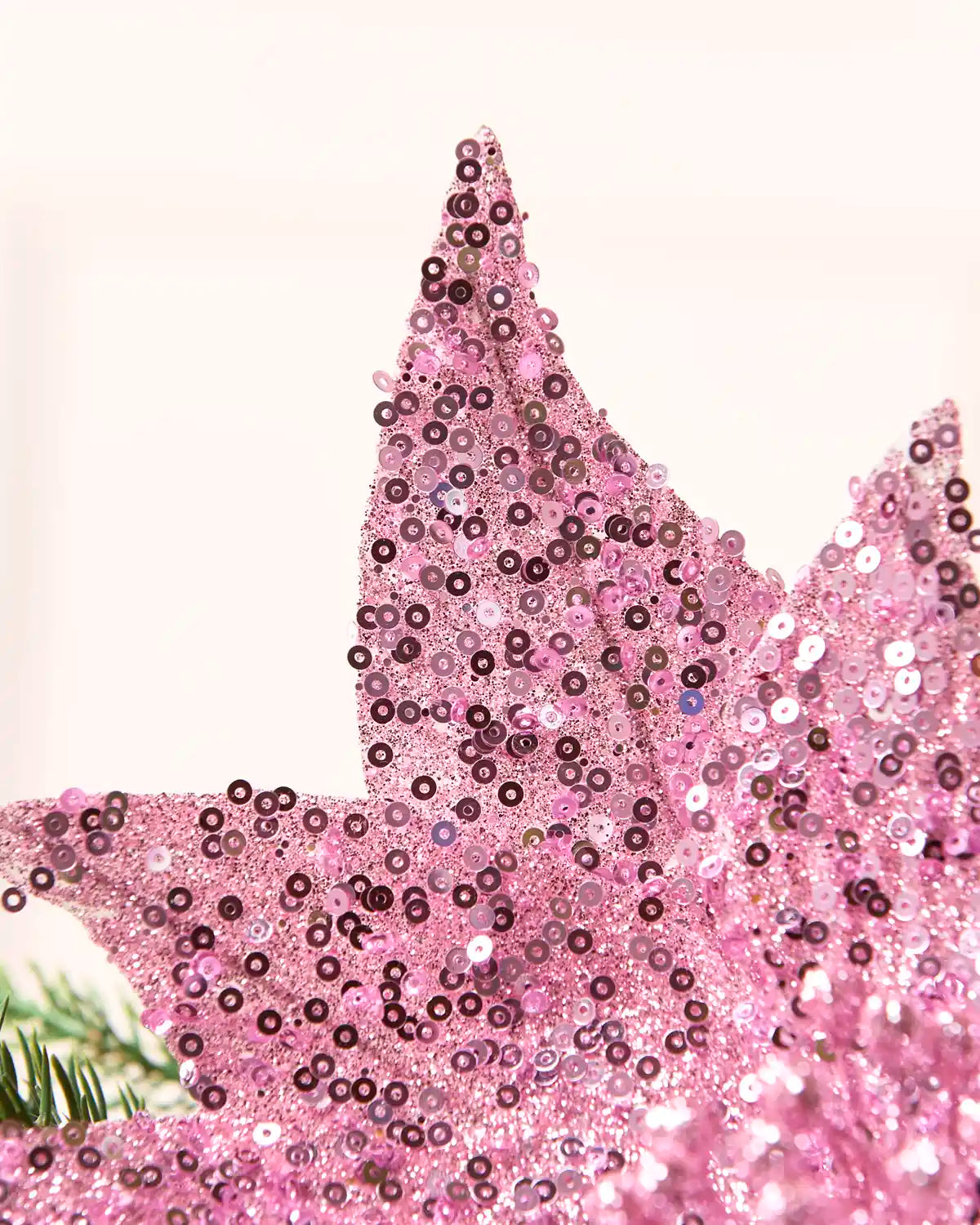 A close-up of a pink sequined decorative object, likely a star topper or embellished accessory, with dense pink and darker purple sequins against a plain light background.