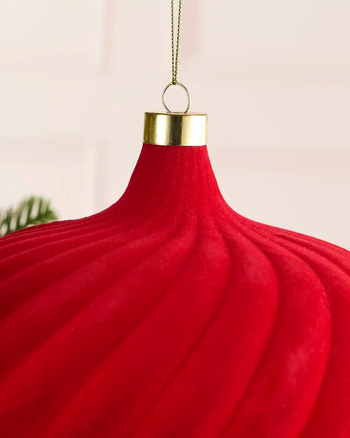 A close-up of a red ribbed Christmas ornament with a gold metal cap and hanging loop, shown against a soft light background.