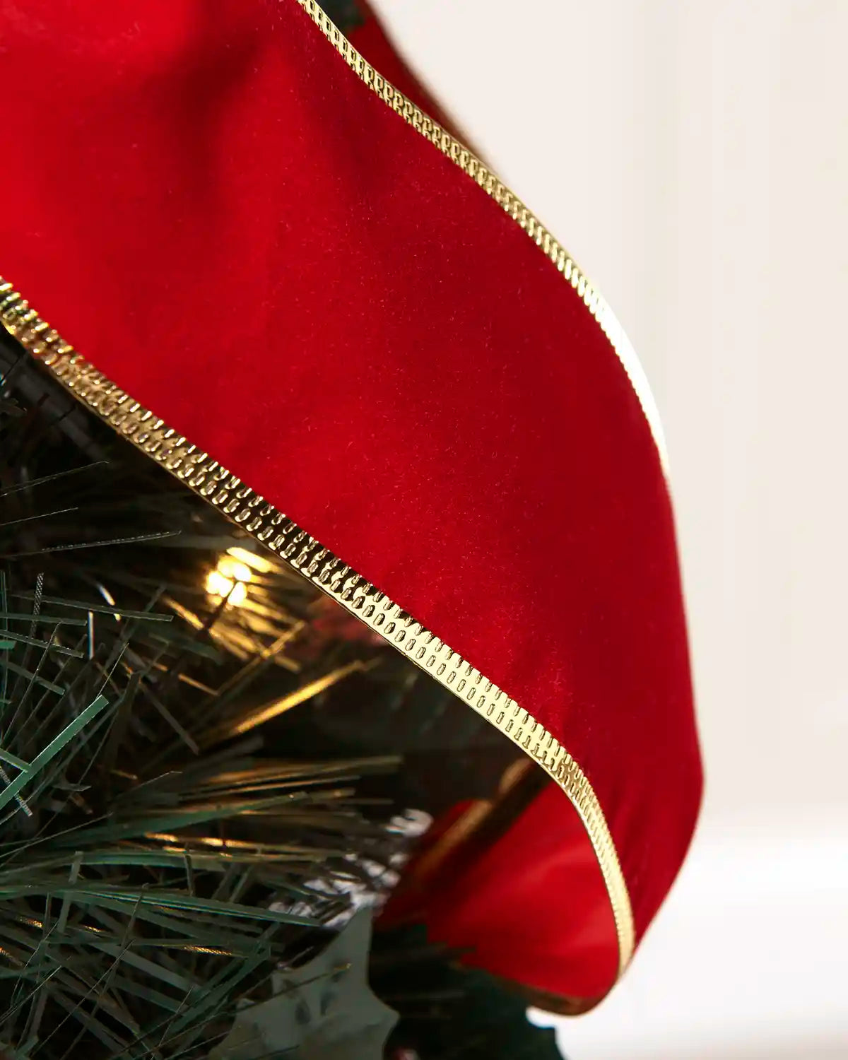 A close-up of a red velvet Christmas tree stocking topper with a decorative gold braided trim, draped over the top of a green artificial Christmas tree.