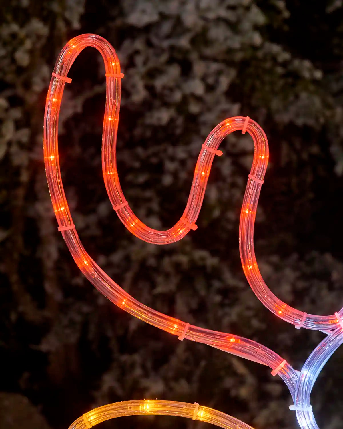 A close-up of a reindeers ear in LED light decoration glowing in red, set against a dark, blurred outdoor background.