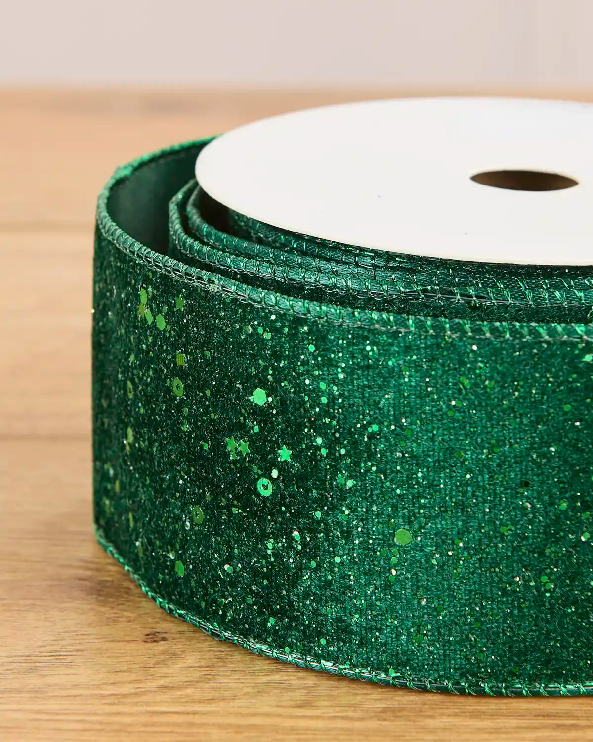 A close-up of a roll of sparkly green glitter ribbon on a wooden surface.