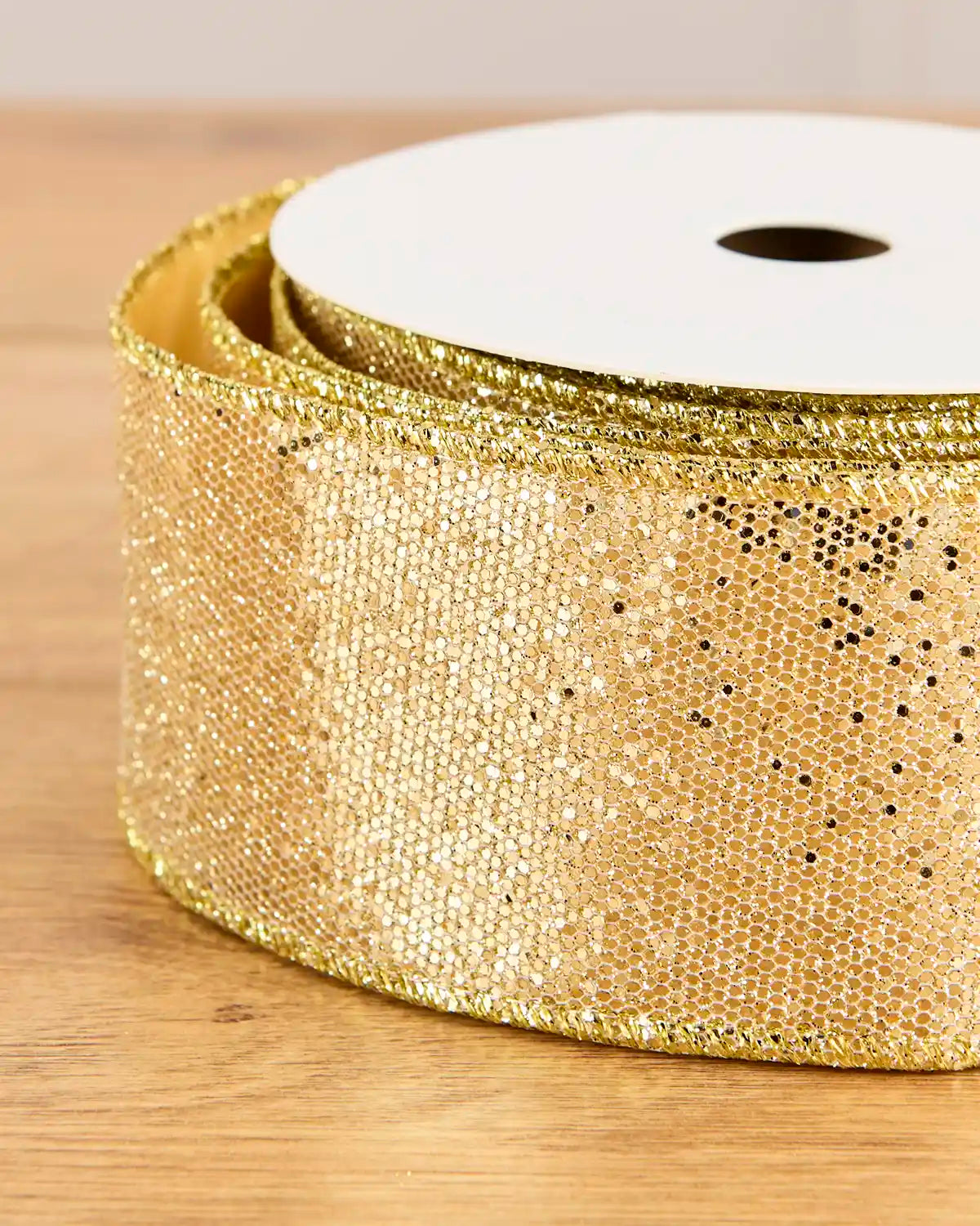 A close-up of a roll of wide, textured gold sequin ribbon on a wooden surface.