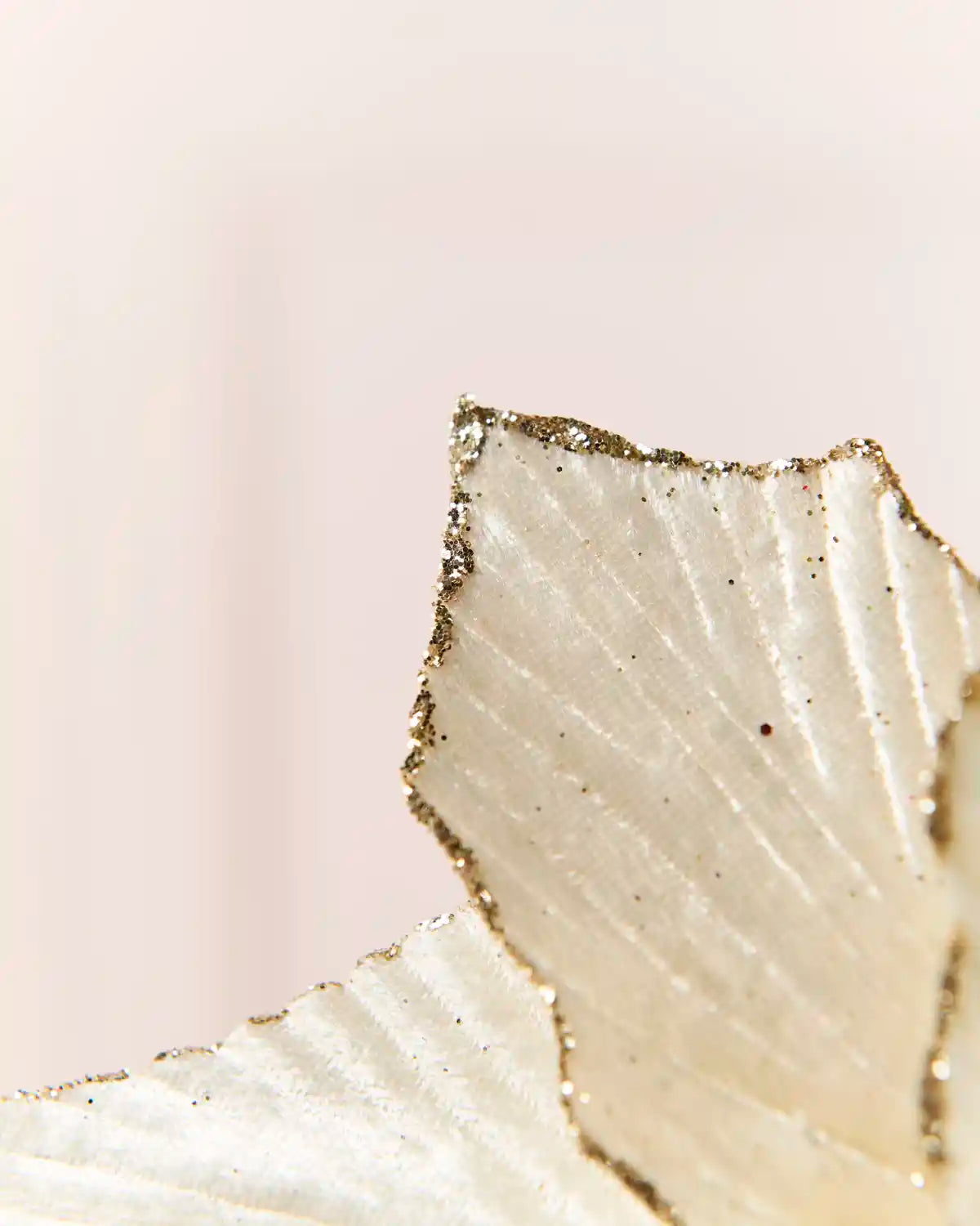 A close-up of a textured, cream ribbed surface with a metallic gold glittery edge, set against a soft, pale pink background.