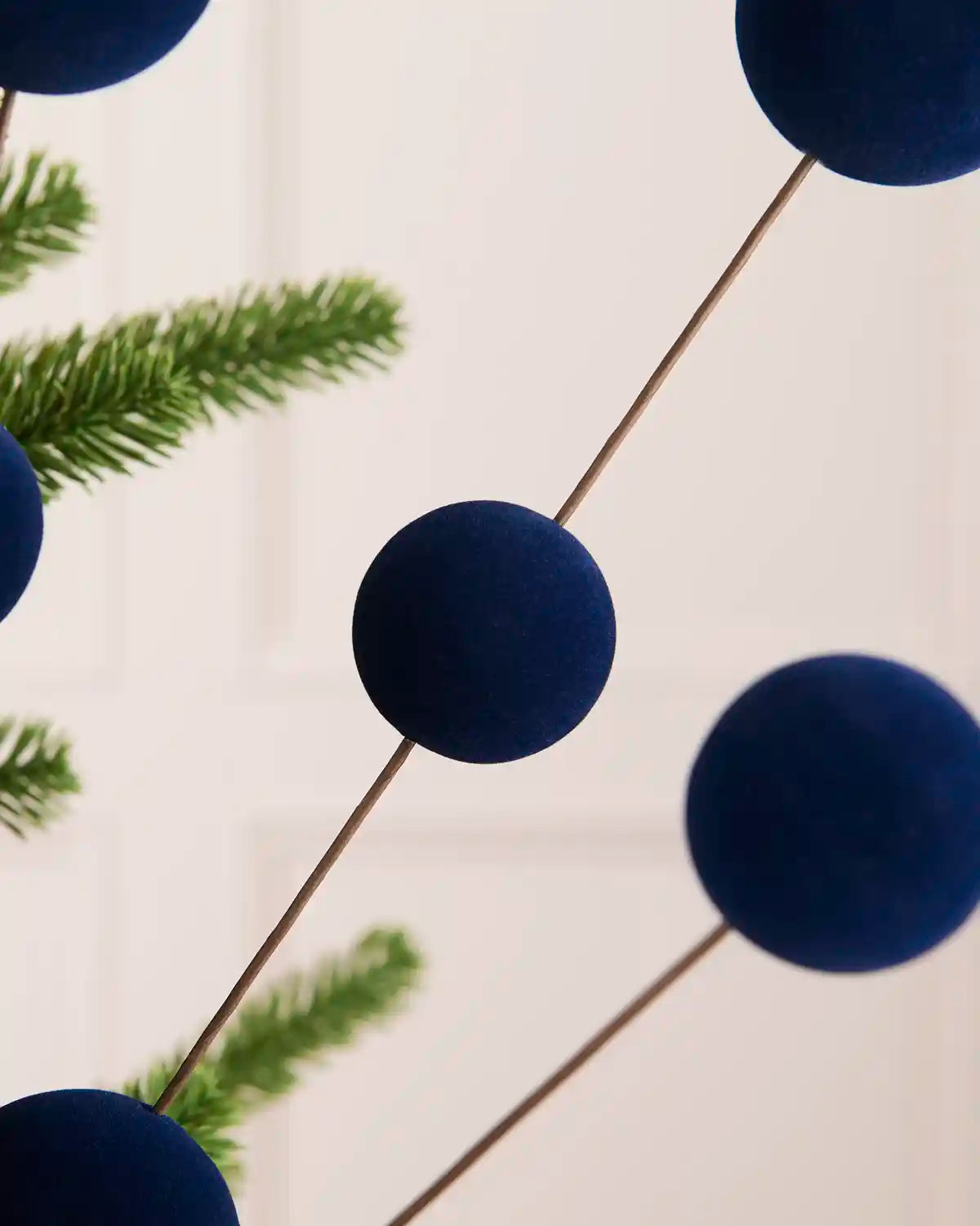 A close-up of a velvet bauble pick with six navy blue velvet ball ornaments on thin stems