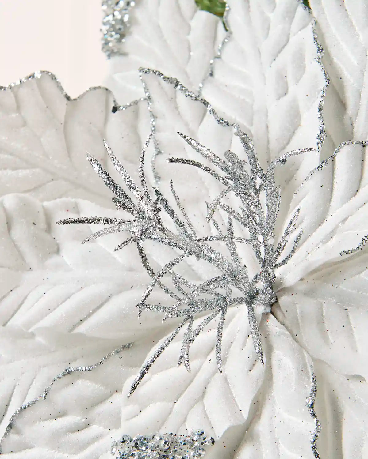 A close-up of a white faux floral poinsettia with large textured petals and glittery silver branch-like accents radiating from the centre.