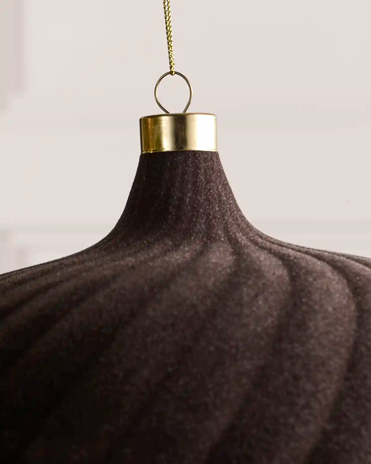 A close-up of an espresso ribbed fabric hanging ornament with a gold metal cap and a gold hanging chain against a light neutral background.