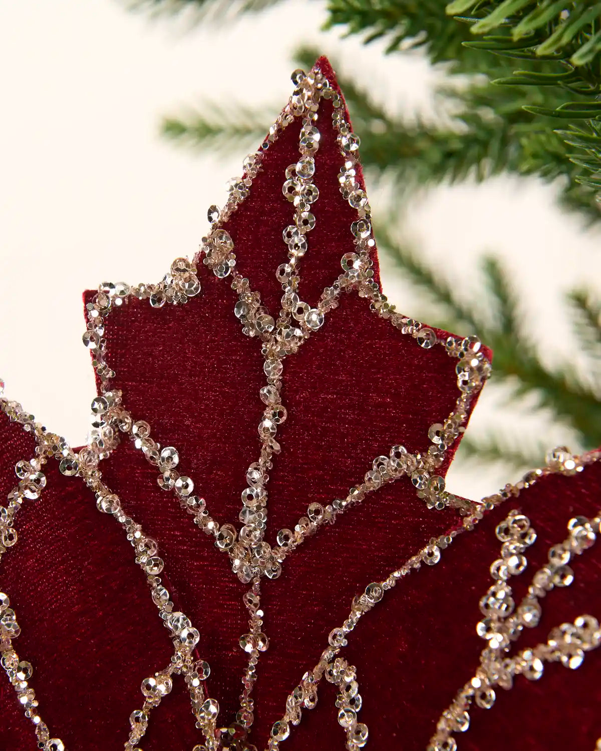 A close-up of top of a Burgundy velvet poinsettia-style decorative flower with Gold rhinestone trim and a glittery gold center.