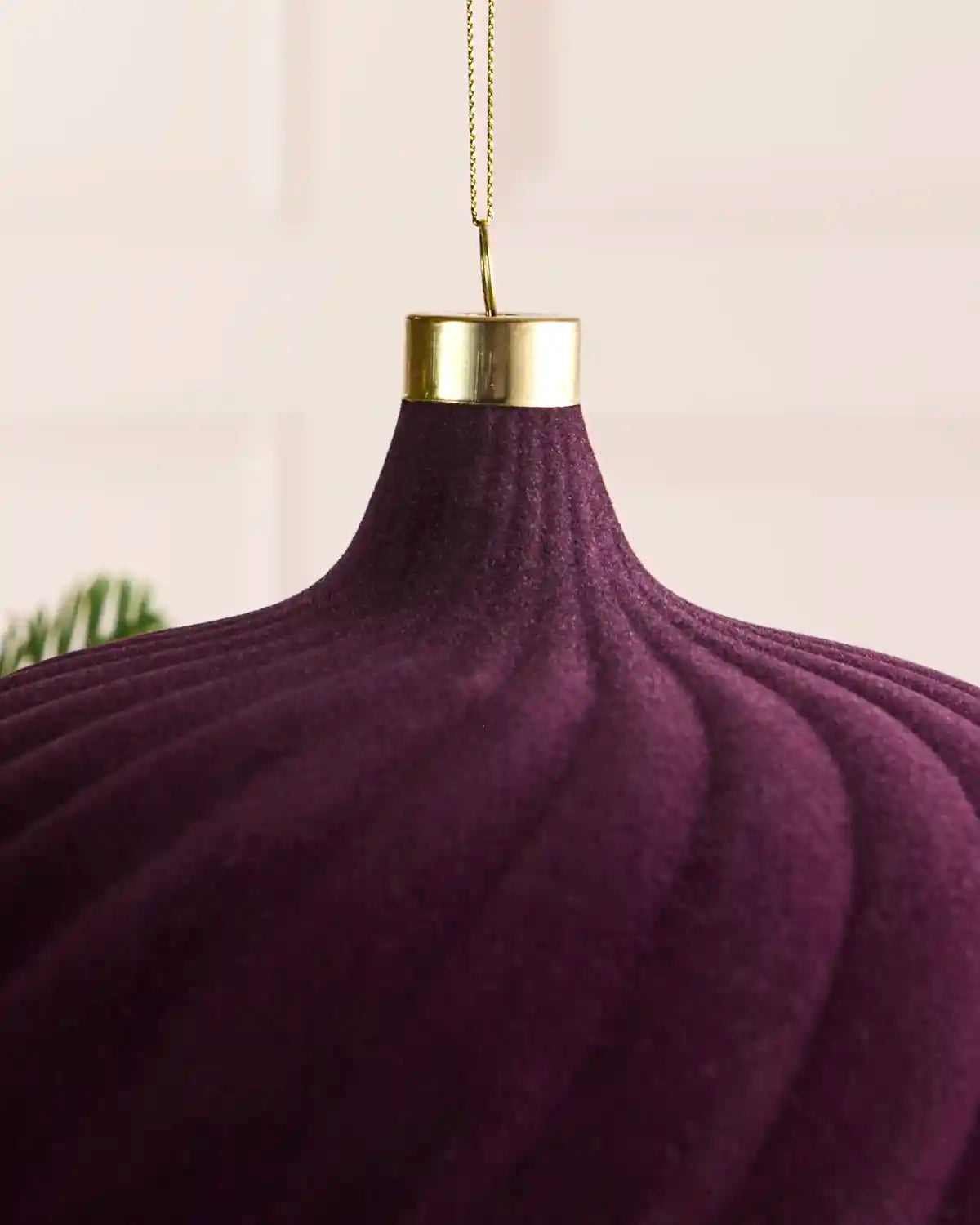 A close up large velvet purple spiral bauble hanging on a Christmas tree with gold string against a light background