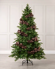 A decorated Christmas tree with green needles and metallic Espresso ornaments, standing on a black metal stand against a white paneled wall.