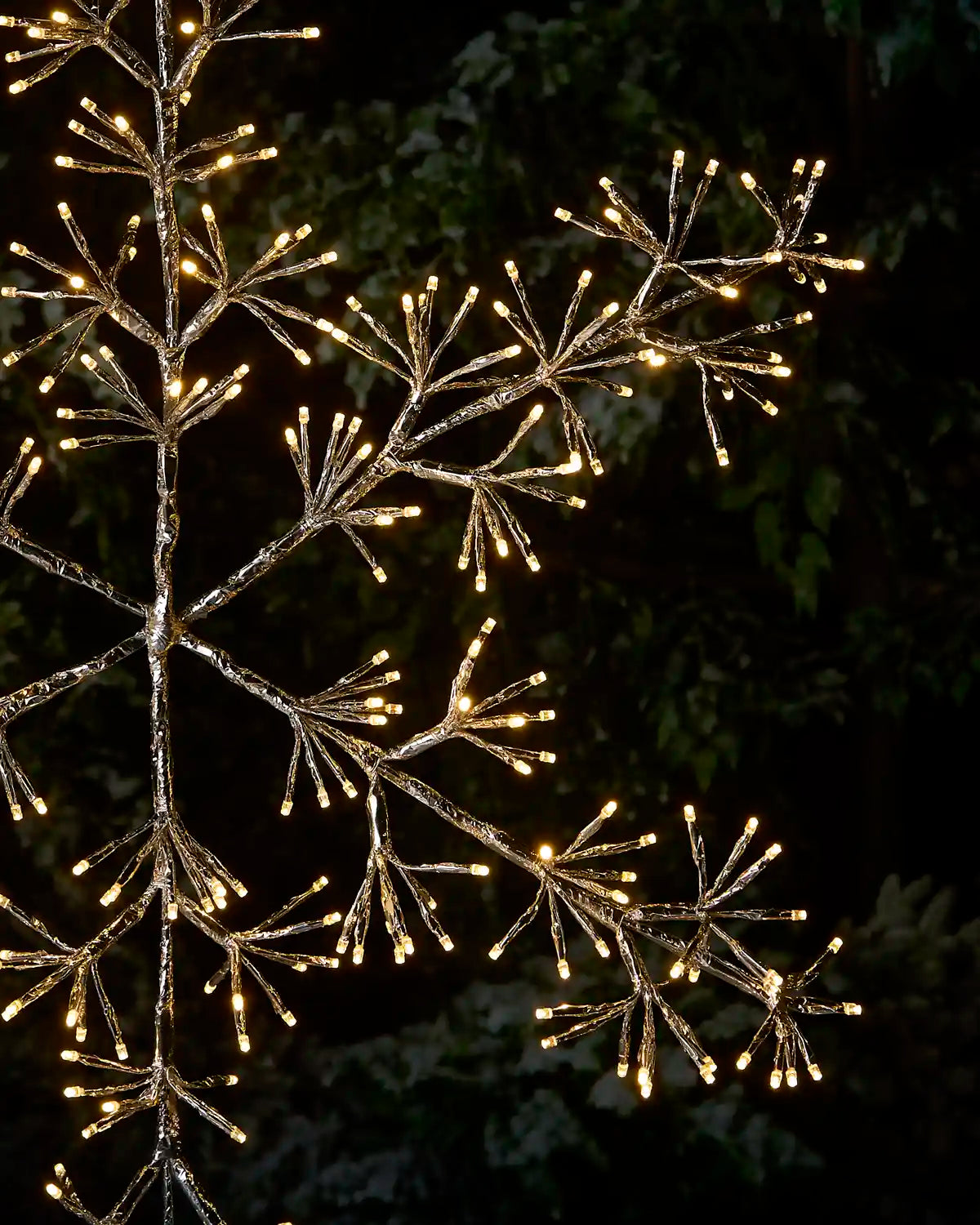 A decorative tree branch light with warm white LED lights on a dark, snowy outdoor background at night.