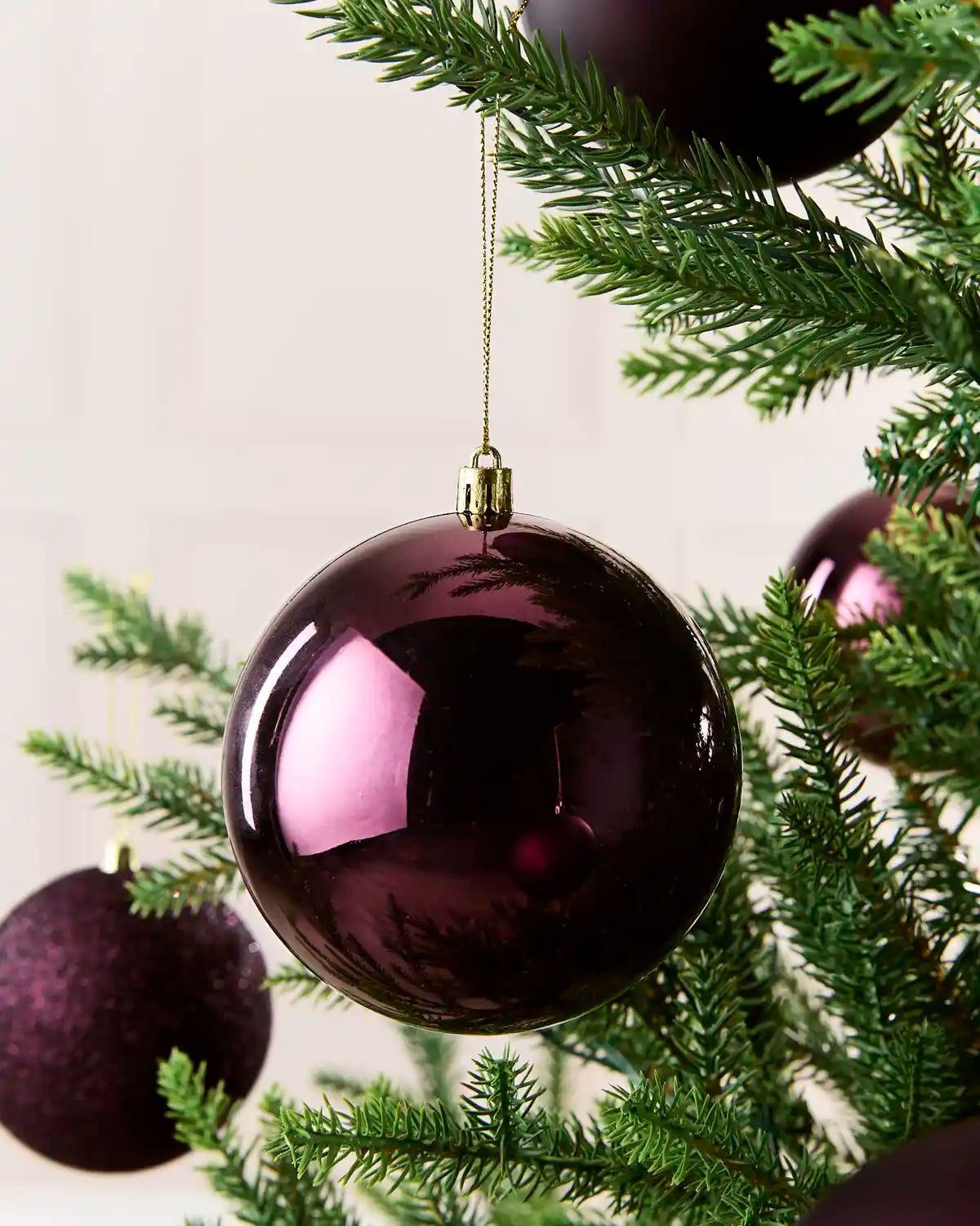 A glossy purple Christmas tree bauble hanging from a green pine tree branch, with other matching purple ornaments partially visible in the background.