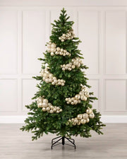 A green artificial Christmas tree decorated with large Latte spherical ornaments, standing on a black metal stand against a white paneled wall and light wood floor.