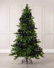 A green artificial Christmas tree decorated with numerous glossy black spherical ornaments, standing on a black metal stand against a light beige paneled wall and light wood floor.