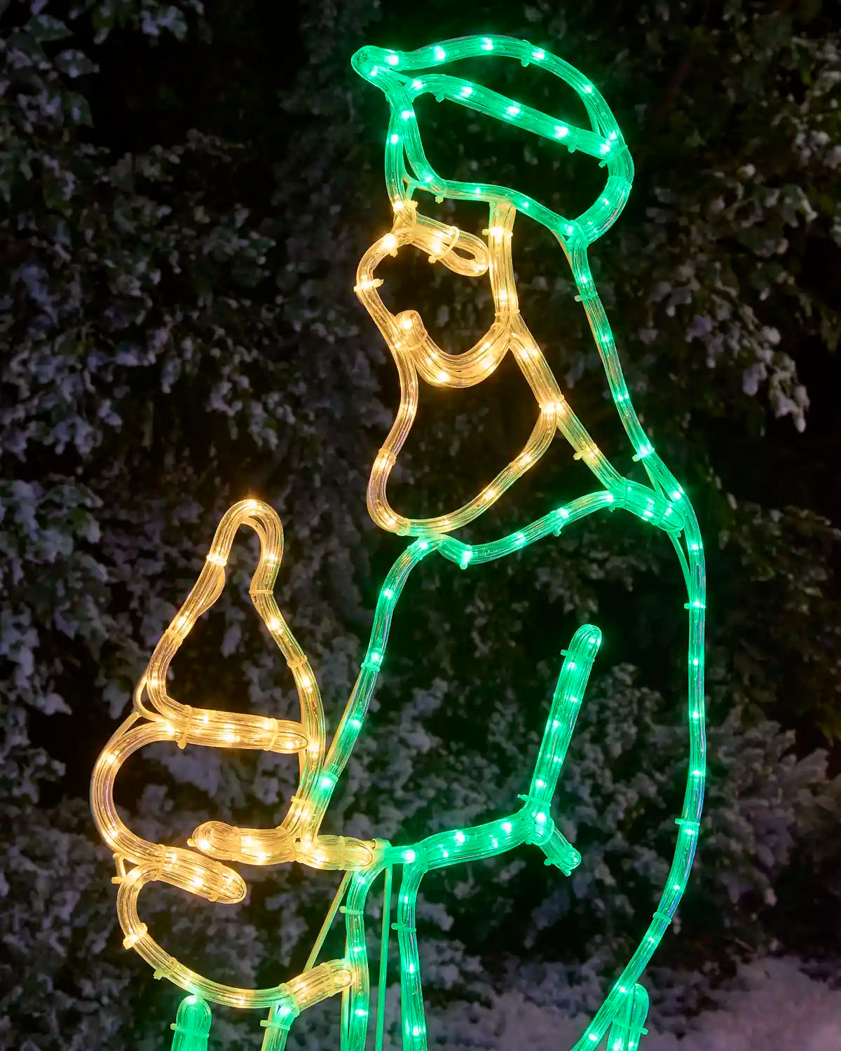 A large Christmas light decoration shaped like a wise, outlined with red LED lights and filled with warm yellow lights, photographed outdoors at night against dark foliage.