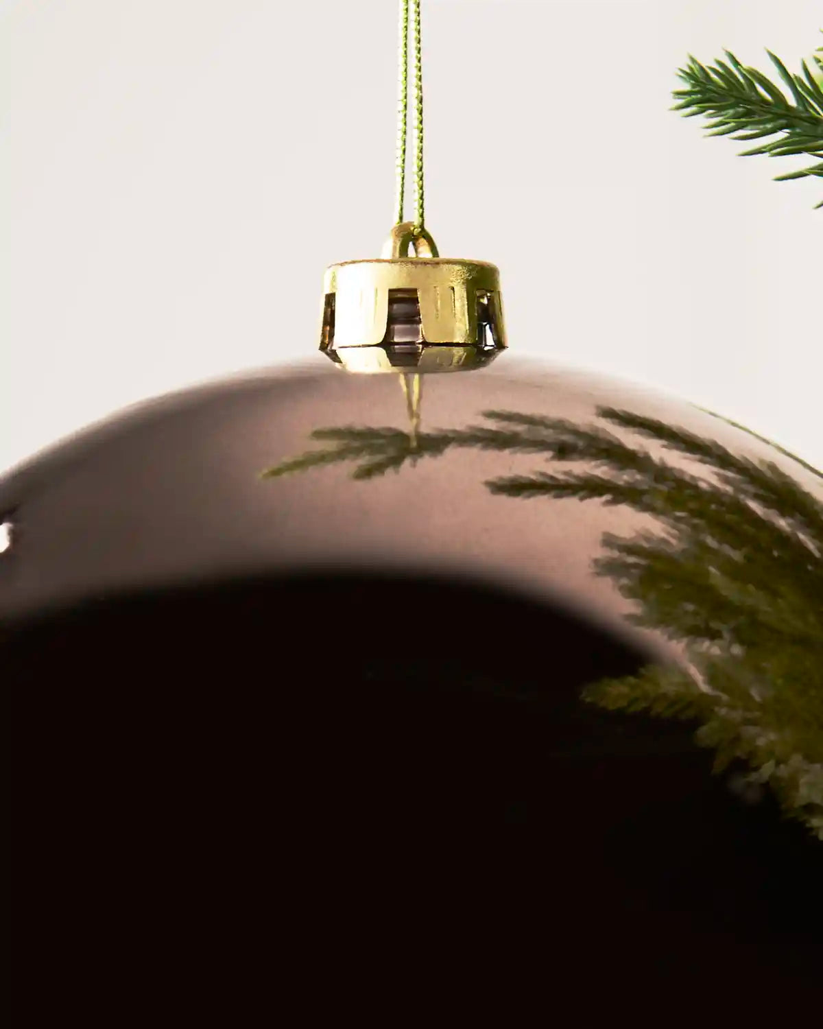 A large, glossy mocha Christmas bauble ornament hanging from a gold cap on a green Christmas tree branch