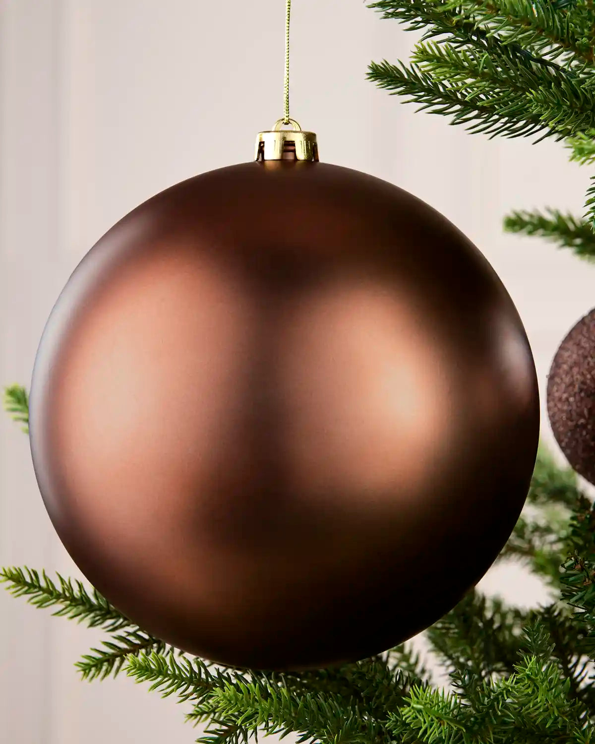 A large matte Espresso Christmas bauble hanging from a green Christmas tree branch against a soft light background.