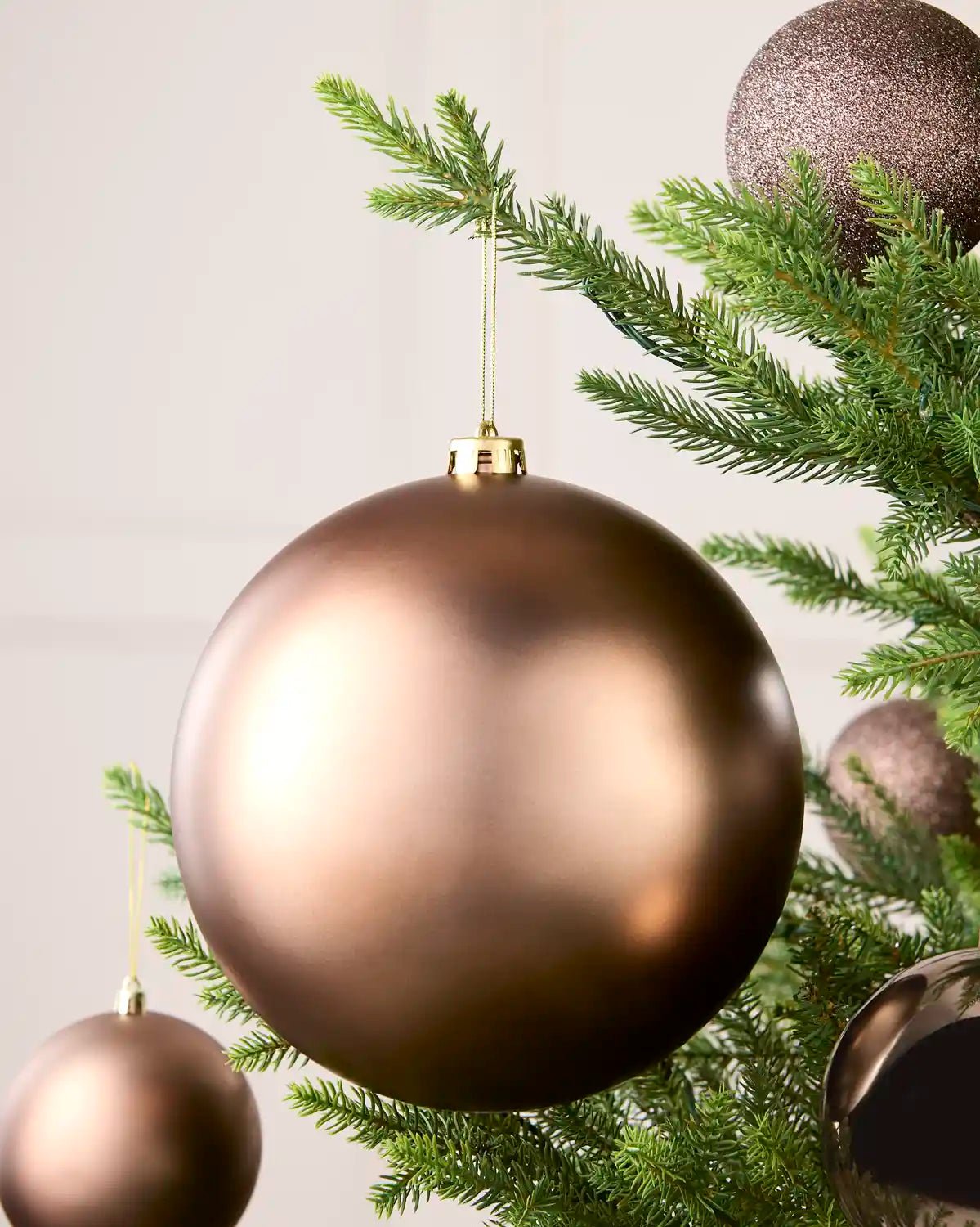 A large metallic Mocha Christmas ornament hanging from green tree branches, with smaller matching ornaments visible in the background.