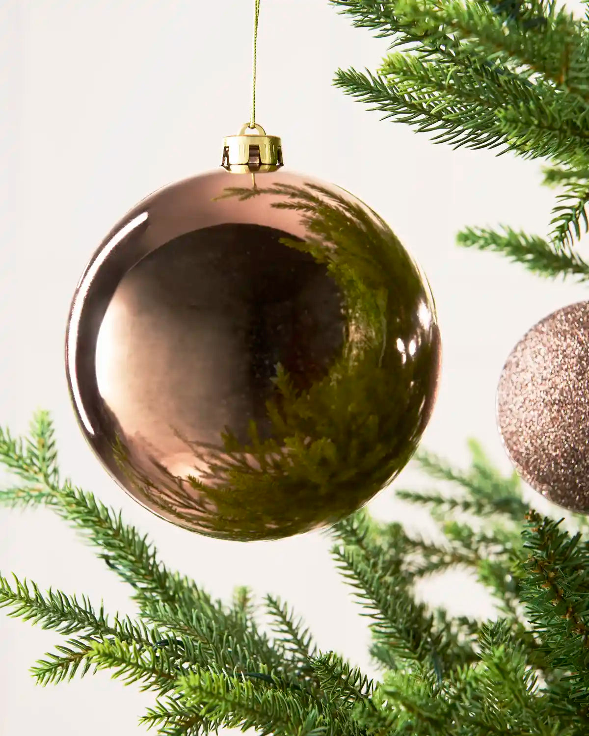 A large, shiny metallic Mocha Christmas ball ornament hanging from a green pine tree branch against a clean white background.