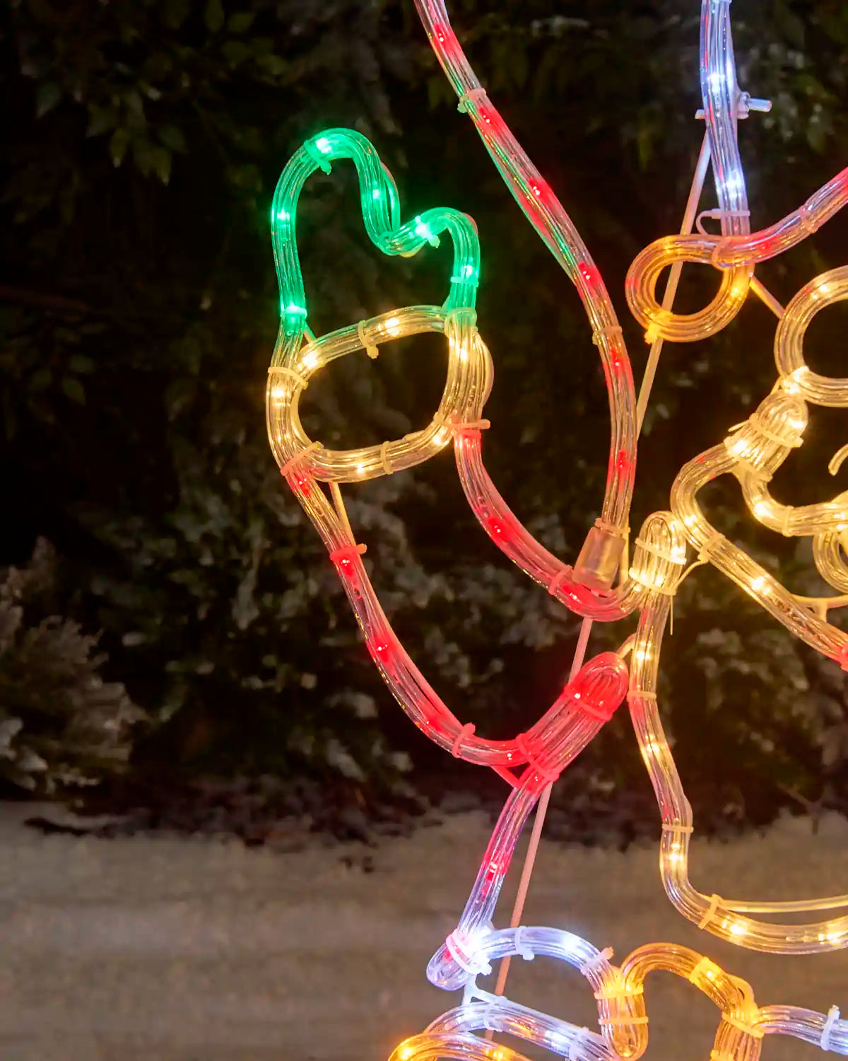 A multicolour LED light Christmas decoration Santa's hand photographed outdoors at night against a dark, leafy background.
