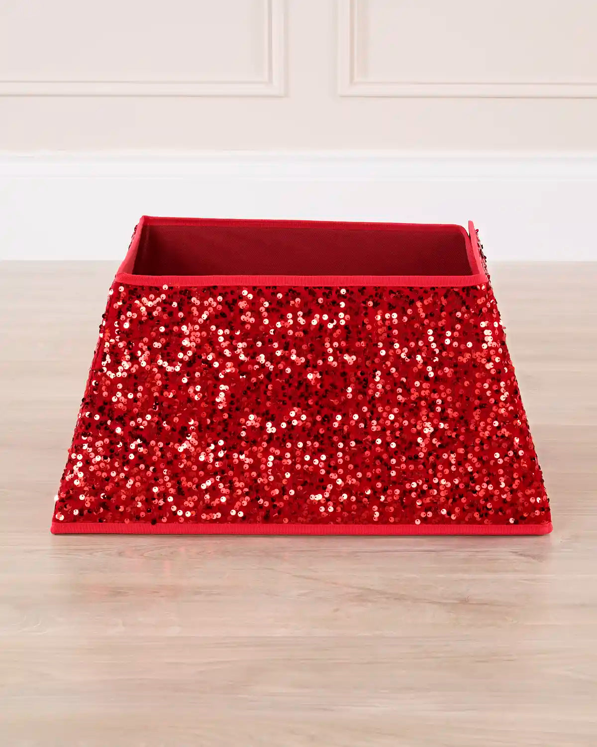 A red sequined square Christmas tree collar on a wooden floor against a light background
