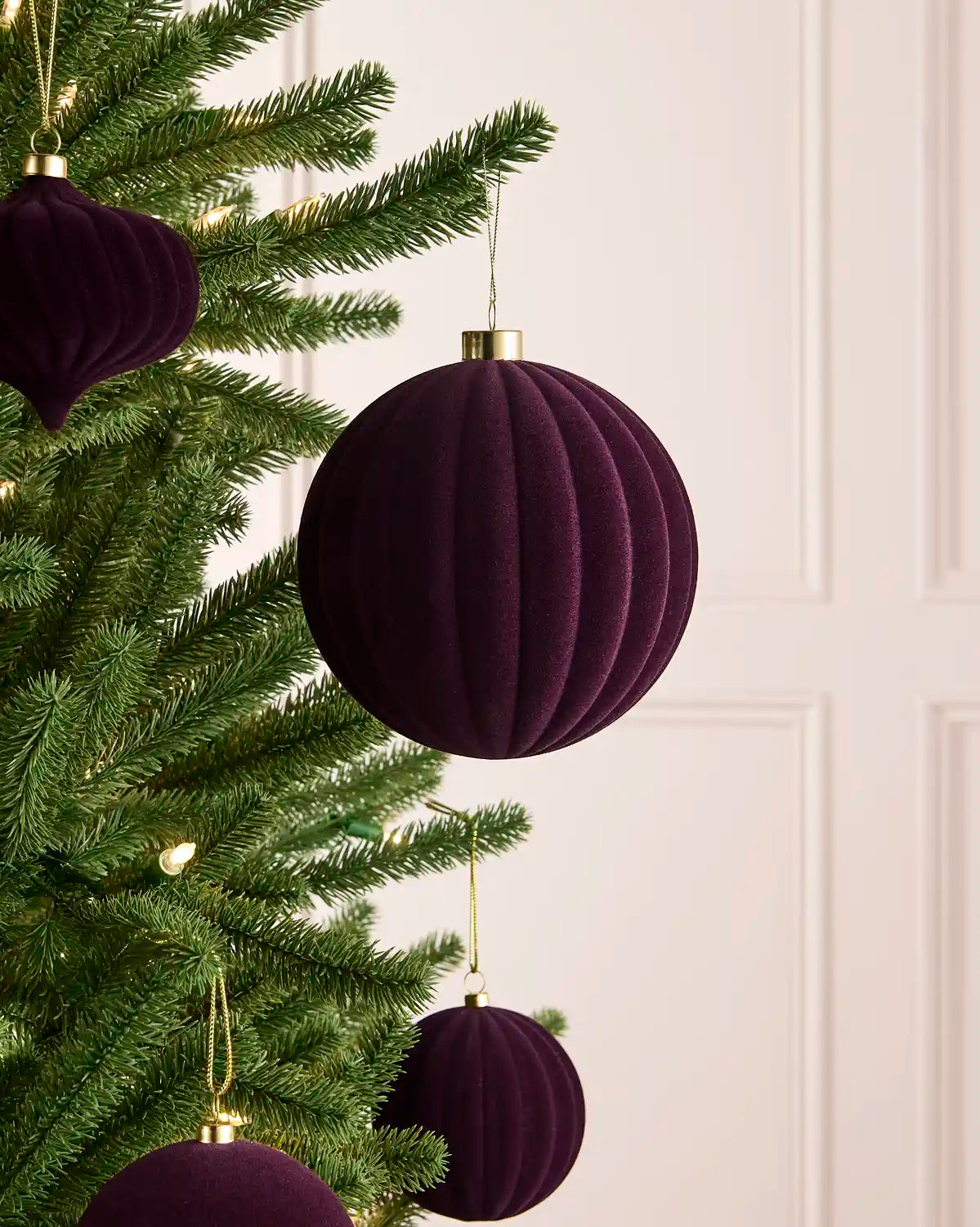 A ribbed purple velvet Christmas ornament hanging from a gold cap with a gold chain against a soft light background.