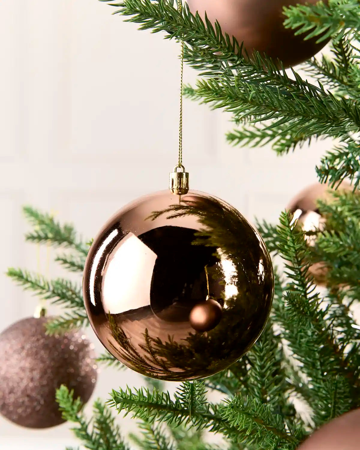 A shiny metallic mocha Christmas ball ornament hanging from a green pine tree branch.