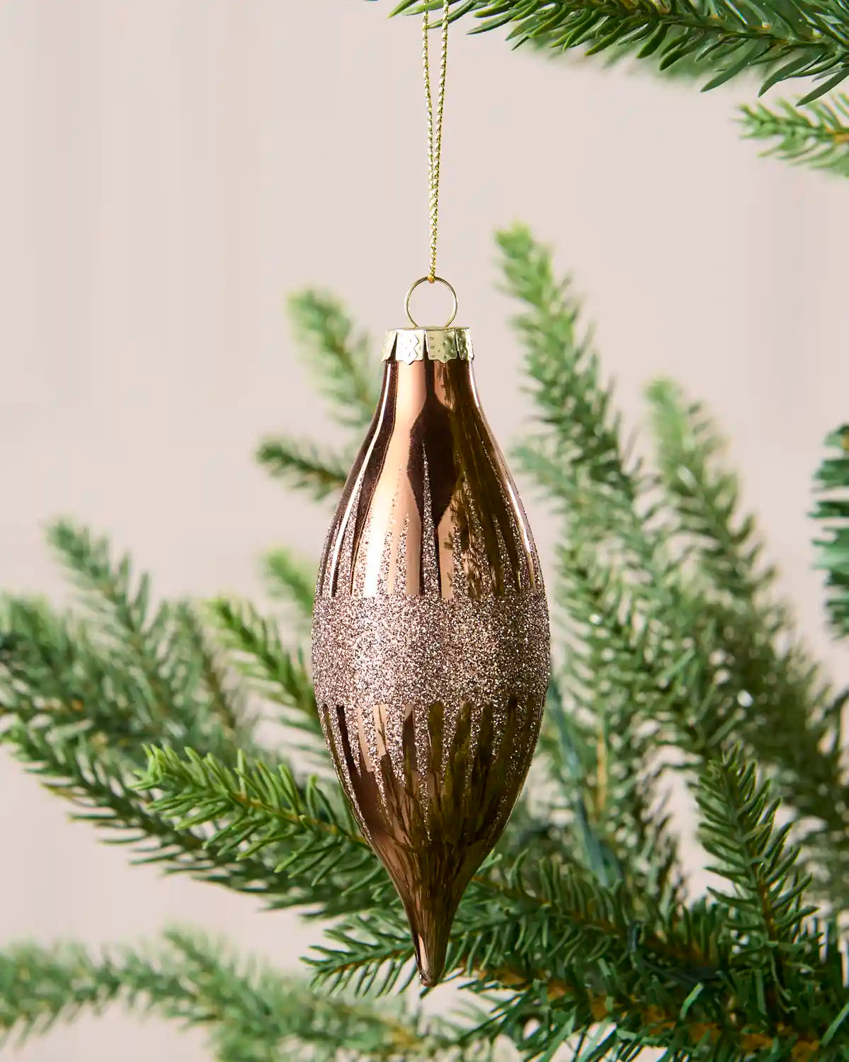 A single Mocha coloured bauble hanging with Gold string on a Christmas tree against a beige background 