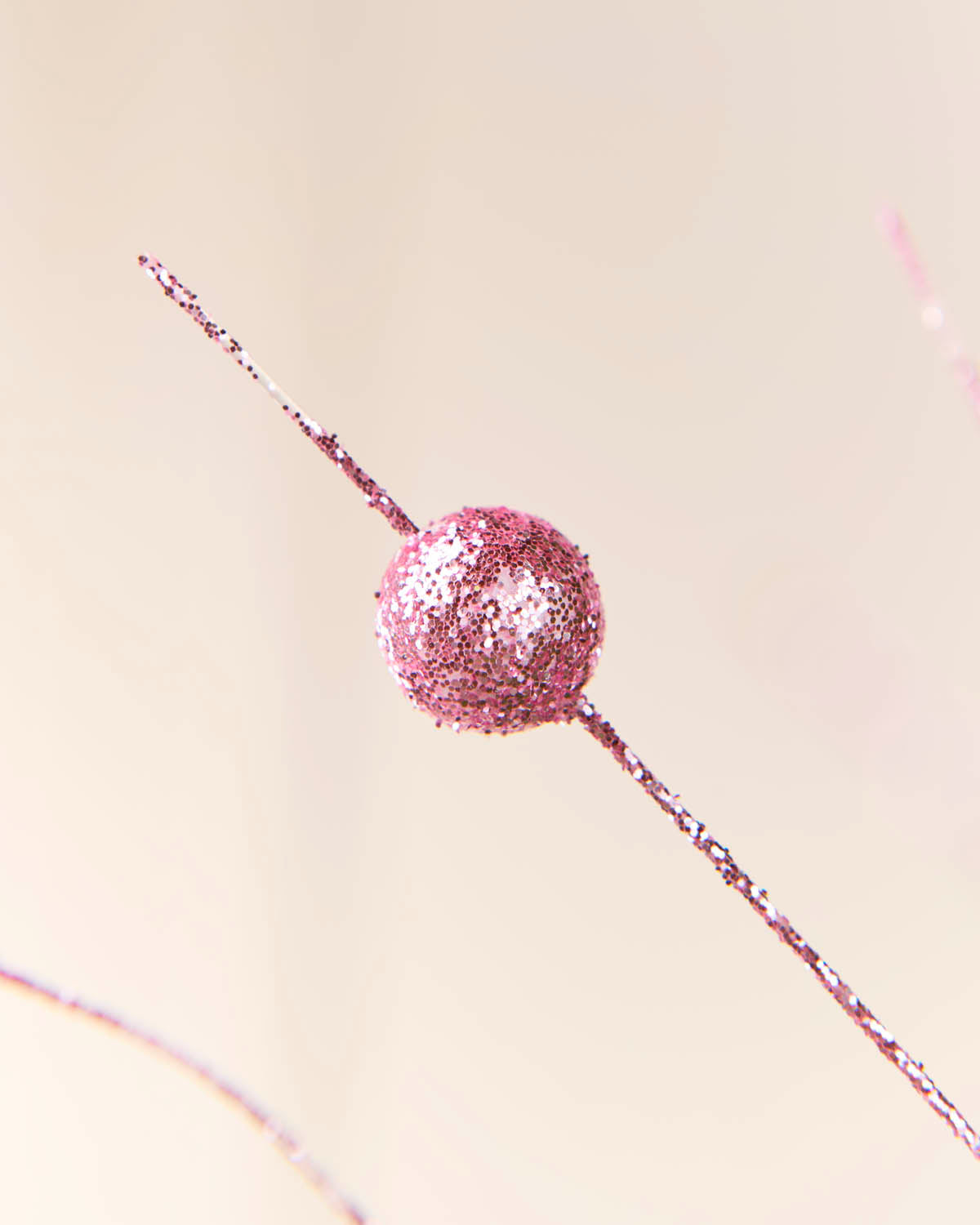 A single round pink glitter bead threaded on a thin metallic pink wire, photographed against a soft warm beige background.