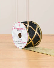 A spool of black ribbon with gold lines in the shape of diamonds on a wooden table against a light background 
