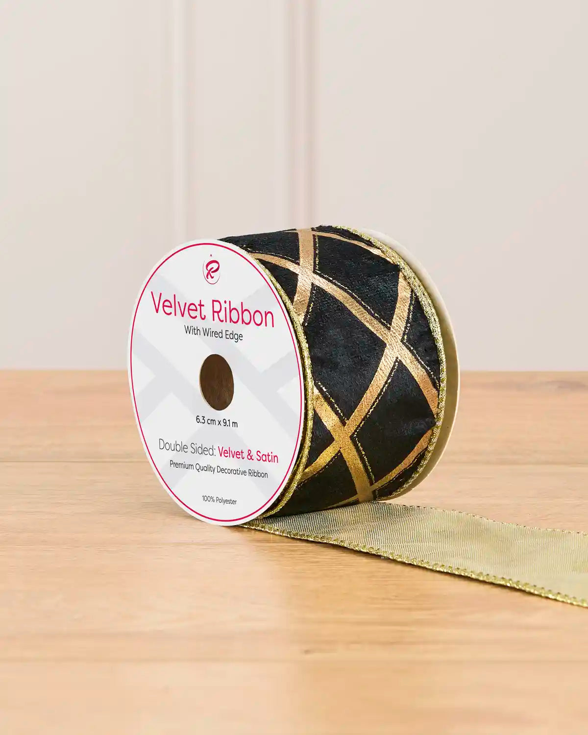 A spool of black ribbon with gold lines in the shape of diamonds on a wooden table against a light background 