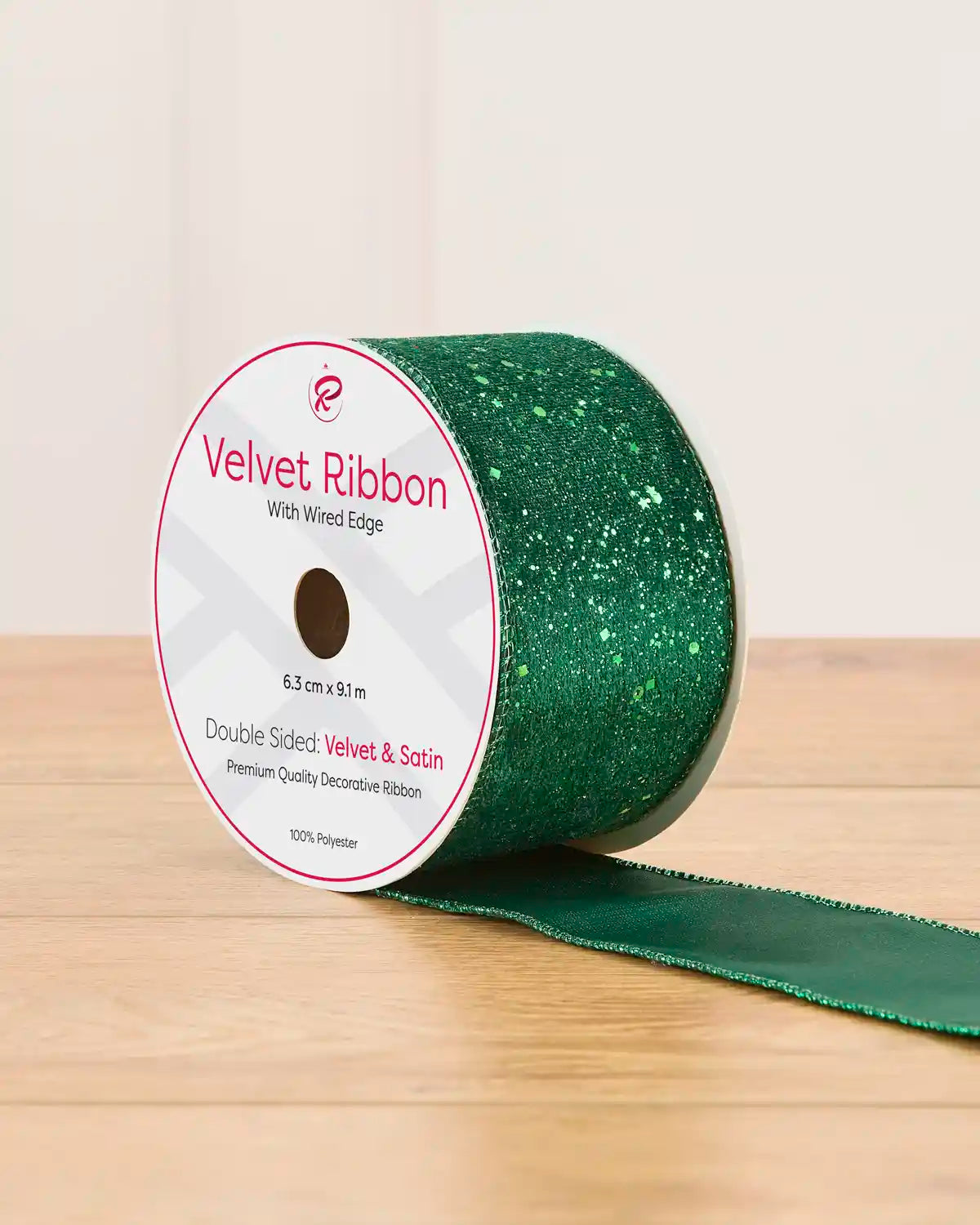 A spool of green sequin ribbon on a wooden table against a light background