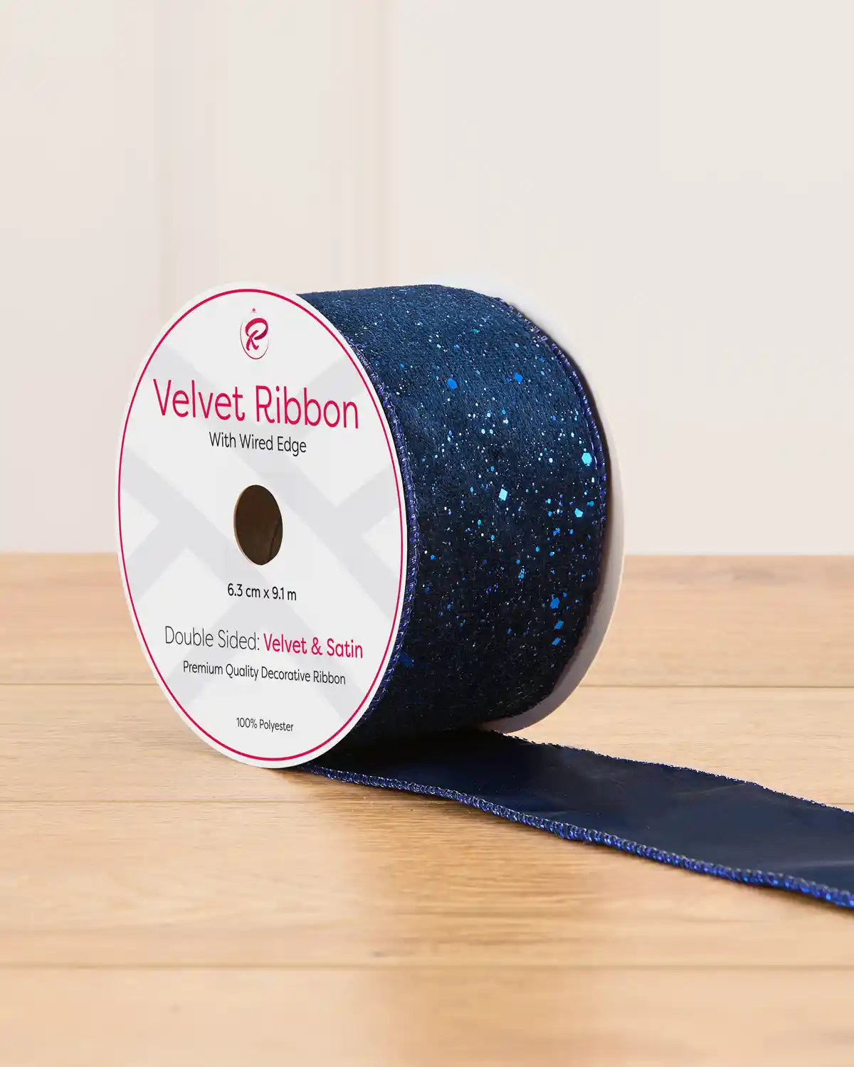 A spool of navy blue ribbon with blue glitter on a wooden table against a light background
