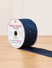 A spool of navy blue ribbon with blue glitter on a wooden table against a light background