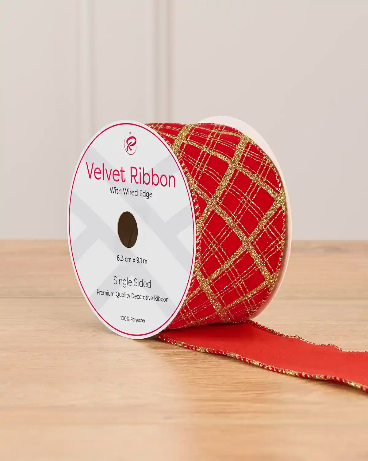 A spool of red ribbon with gold lines on a wooden table against a light background 
