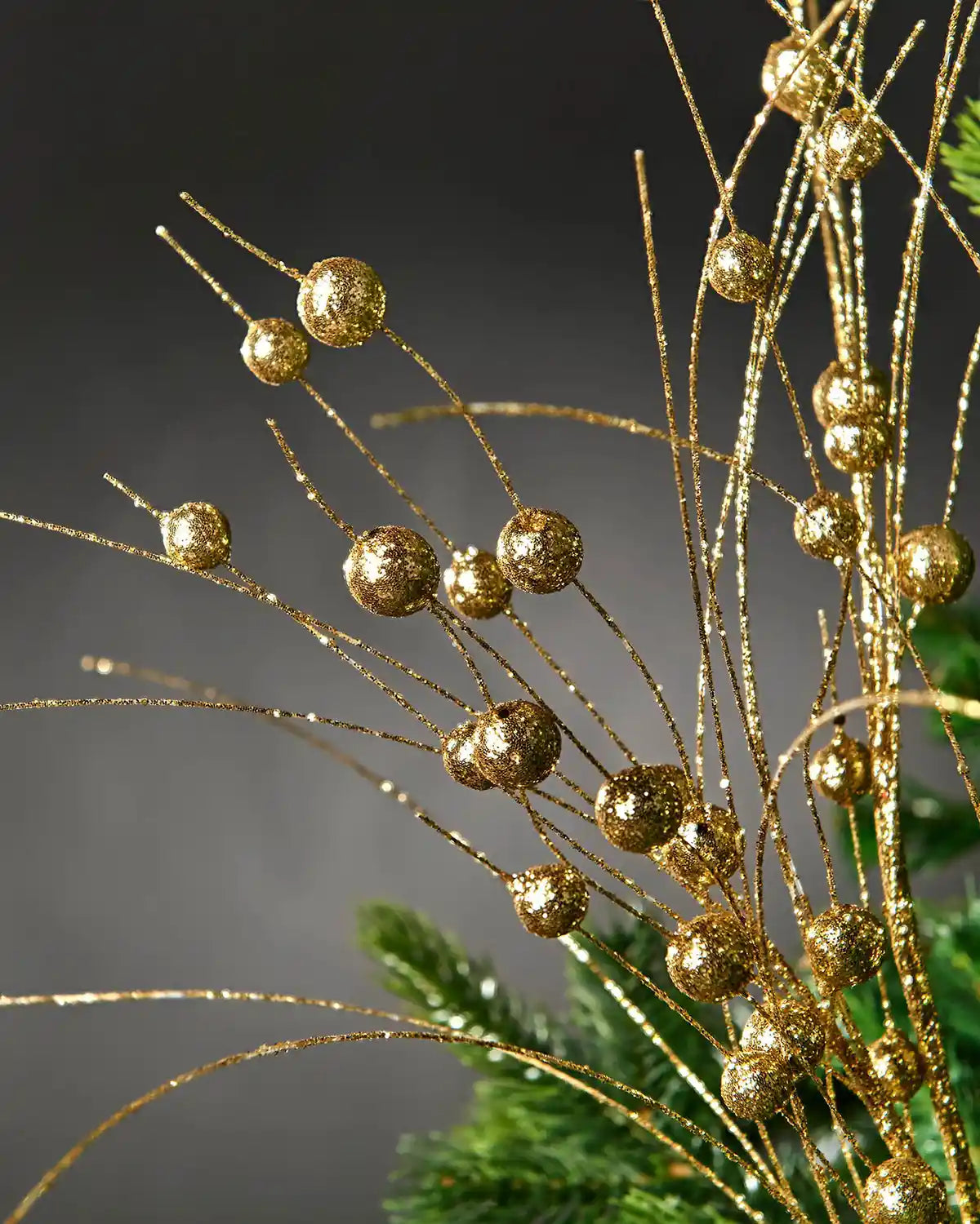 Additional close-up of the gold berry spray decoration attached to a Christmas tree in front of grey wall background highlighting glitter effect