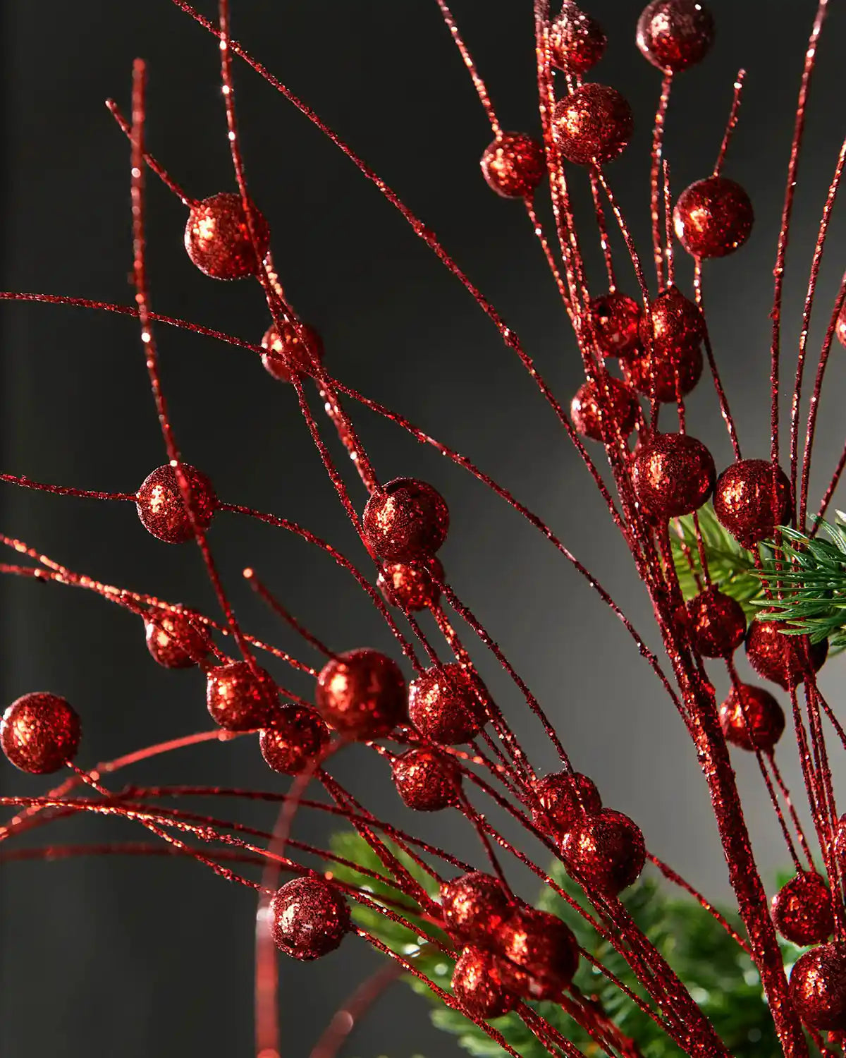Additional close-up of the red glitter berries spray attached to Christmas tree in front of grey wall background