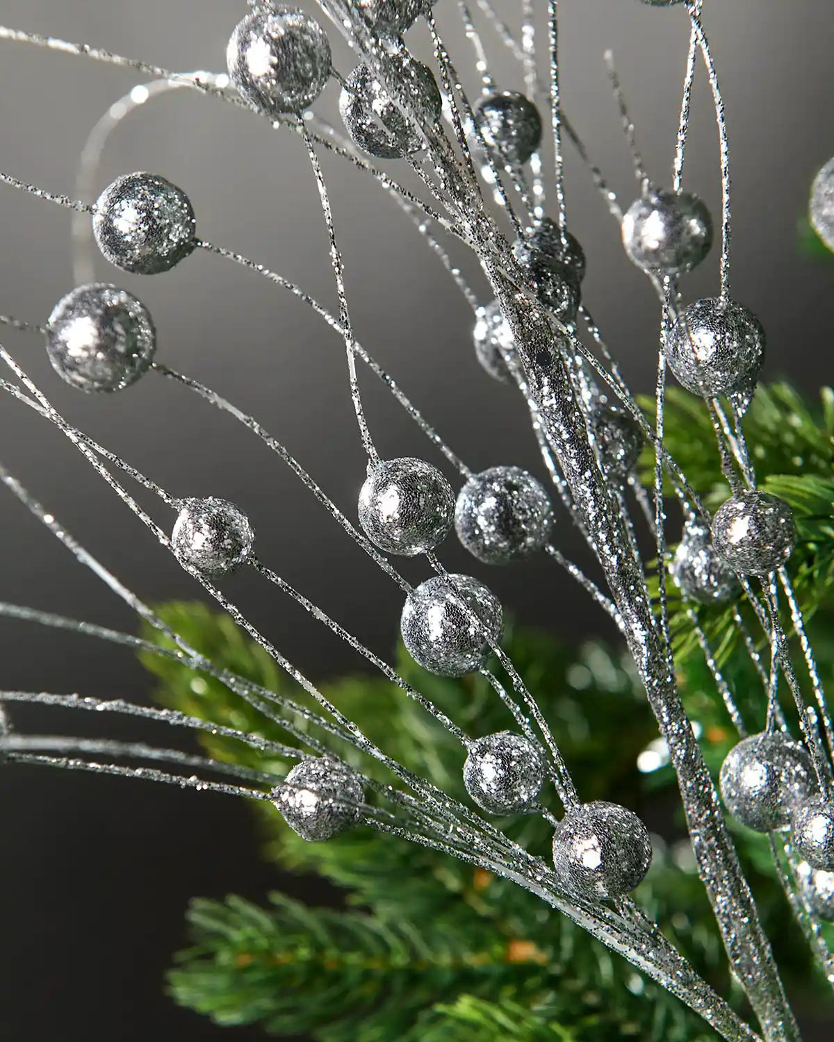 Additional close-up of silver glitter berries spray attached to Christmas tree in front of grey wall background