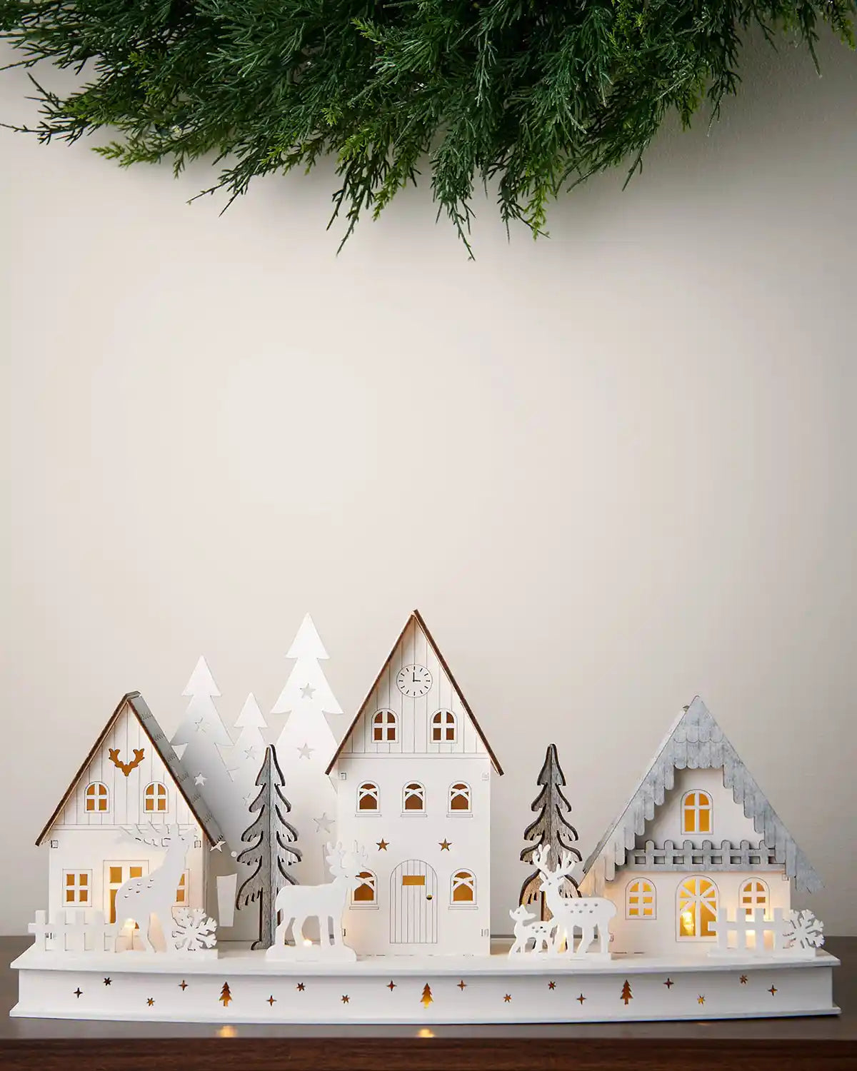 Alternative full image of 40cm pre-lit white wooden village scene with warm white light on dark surface with white walls