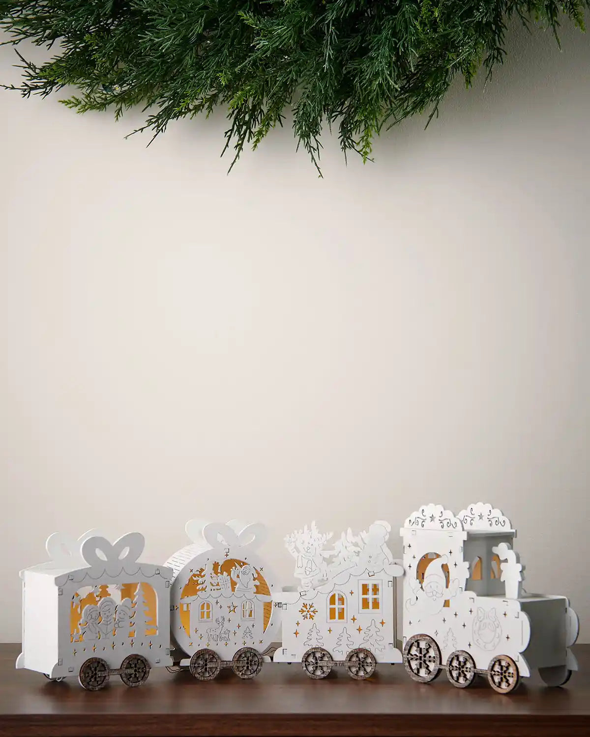 Alternative full image of pre-lit white wooden train decoration with warm white light on dark surface in front of white wall